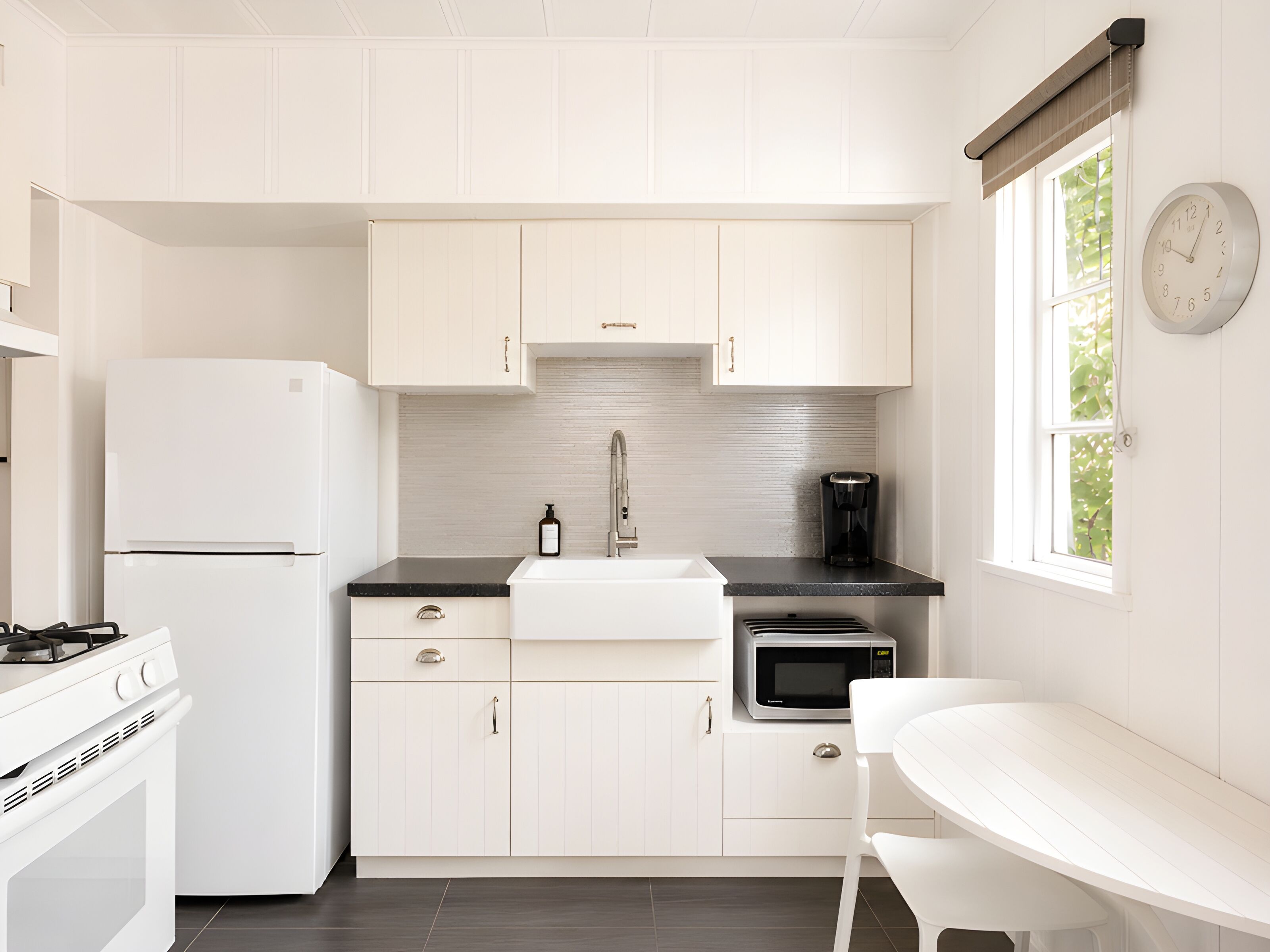 Une cuisine moderne avec des meubles blancs, un plan de travail noir, un évier, une cuisinière, un four et un four à micro-ondes.