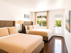 Habitación de hotel con dos camas, una mesita de noche, una lámpara, una puerta con vistas y un cuadro en la pared.