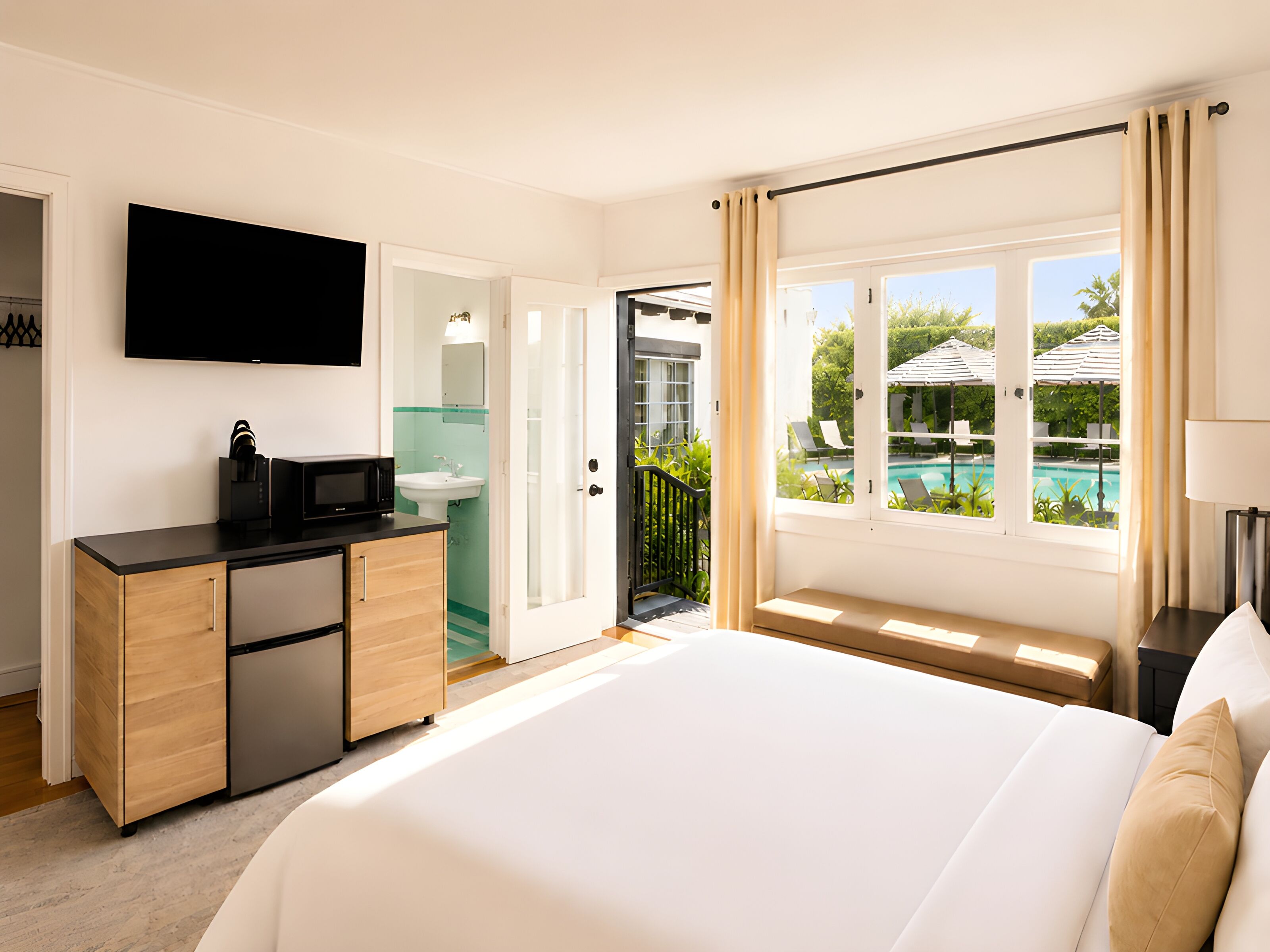 Habitación de hotel con cama, escritorio con microondas, lavamanos, televisor y vista a una piscina.