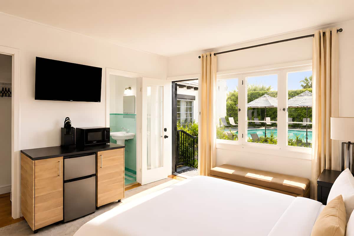 A hotel room with a bed, a desk with a microwave, a sink, a TV, and a view of a pool.