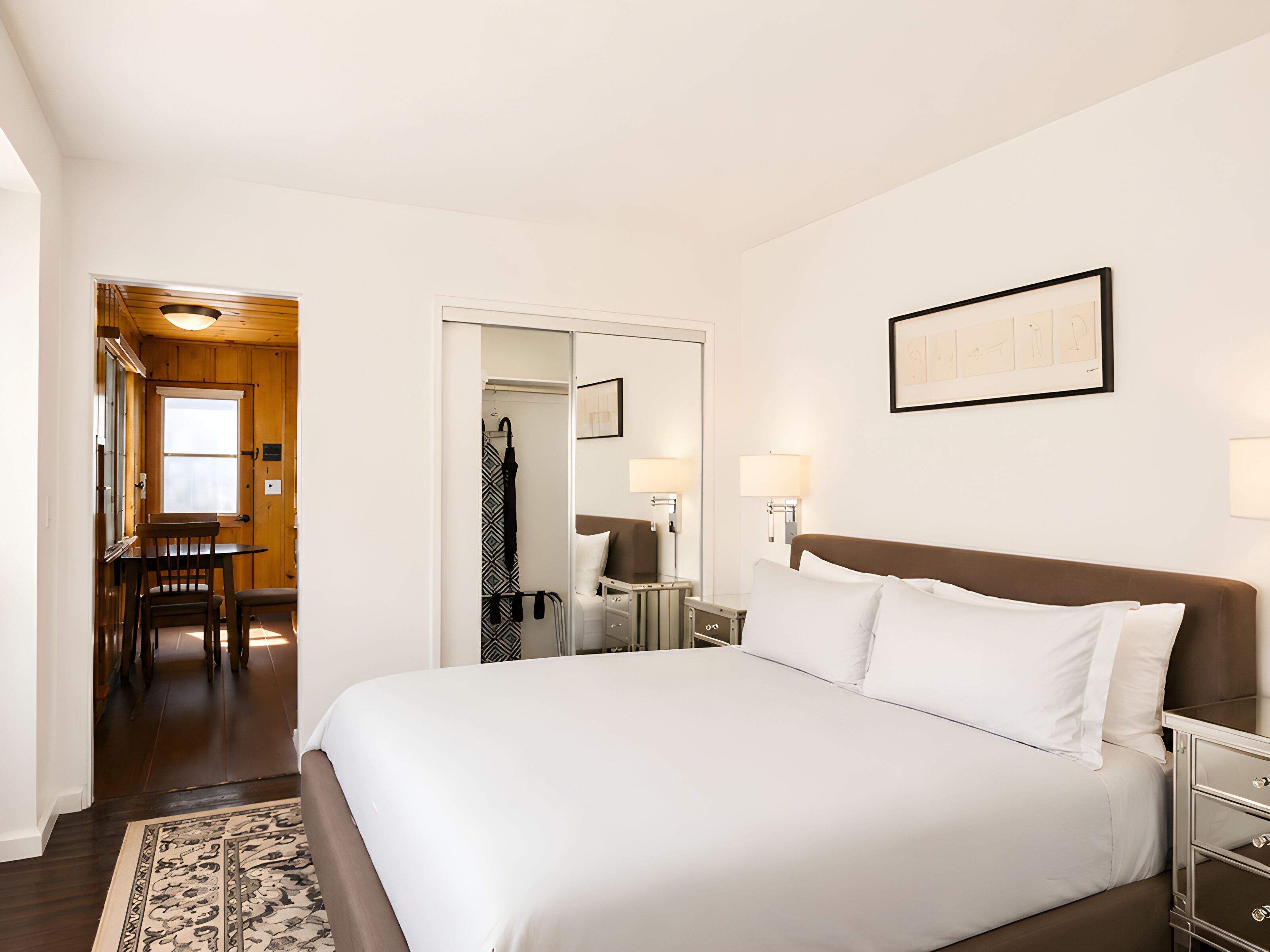 Un cuarto de hotel con una cama grande, mesitas de noche, un escritorio con una silla, un espejo y un cuadro en la pared.
