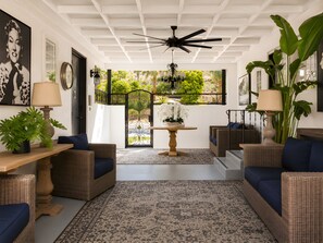 Una habitación con muebles de mimbre, ventilador de techo, una planta en maceta y vistas a través de un ventanal.