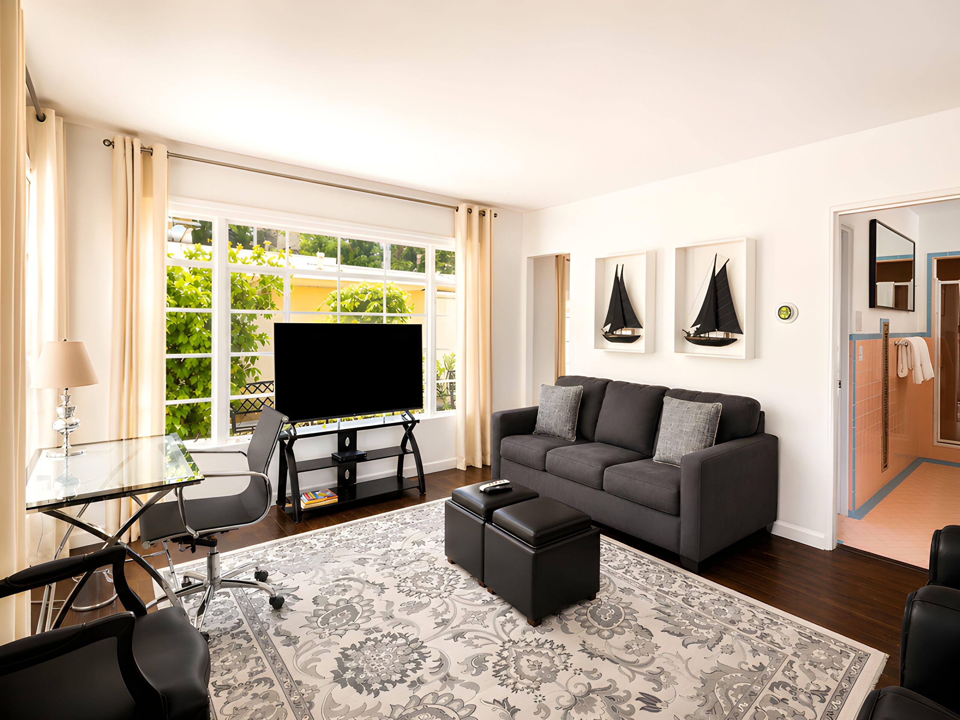 A modern living room with a flat-screen TV, a grey sofa, a coffee table, and a patterned rug.