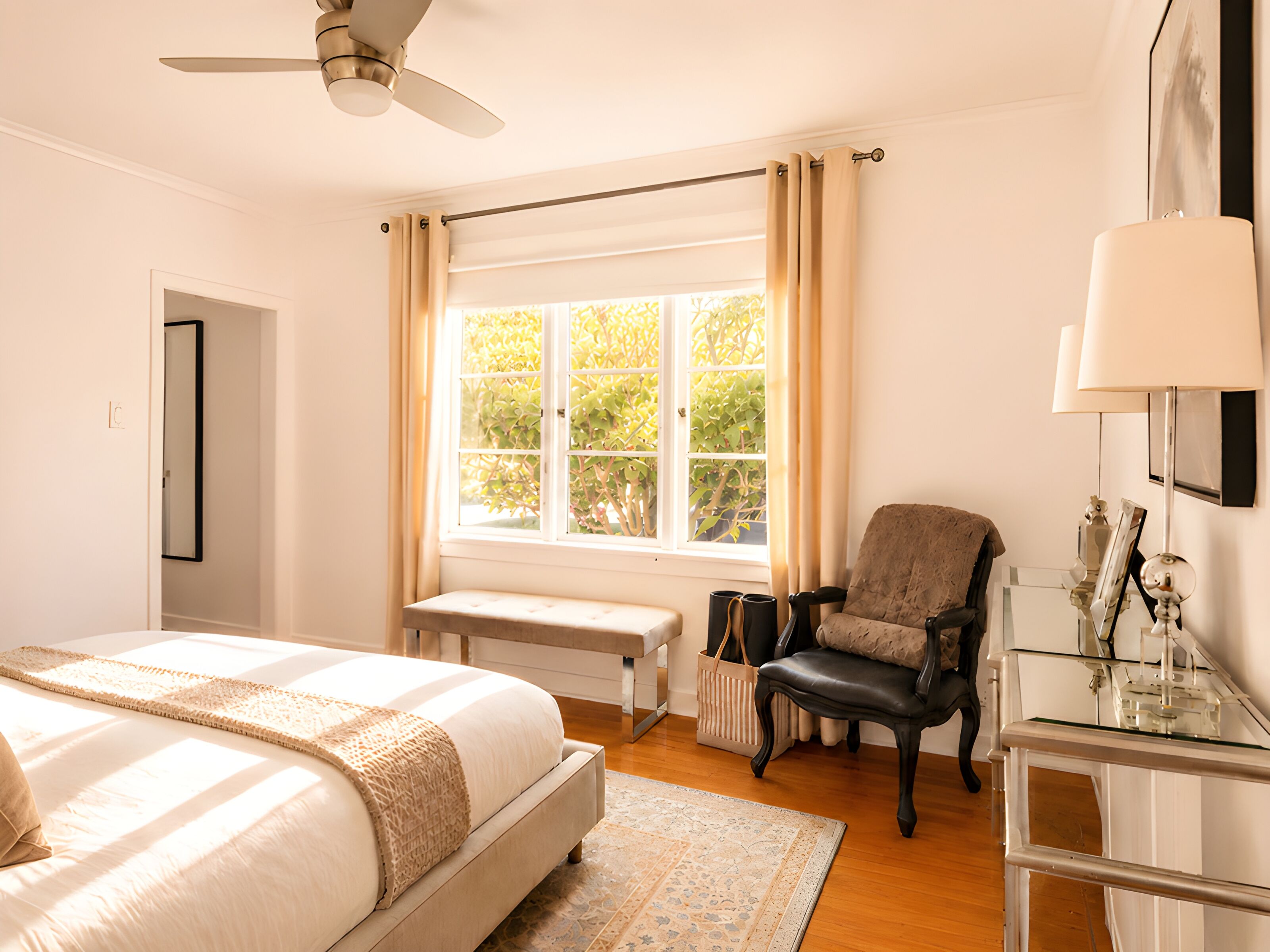 Un dormitorio con cama, una silla, un escritorio, una ventana con cortinas y un ventilador de techo.