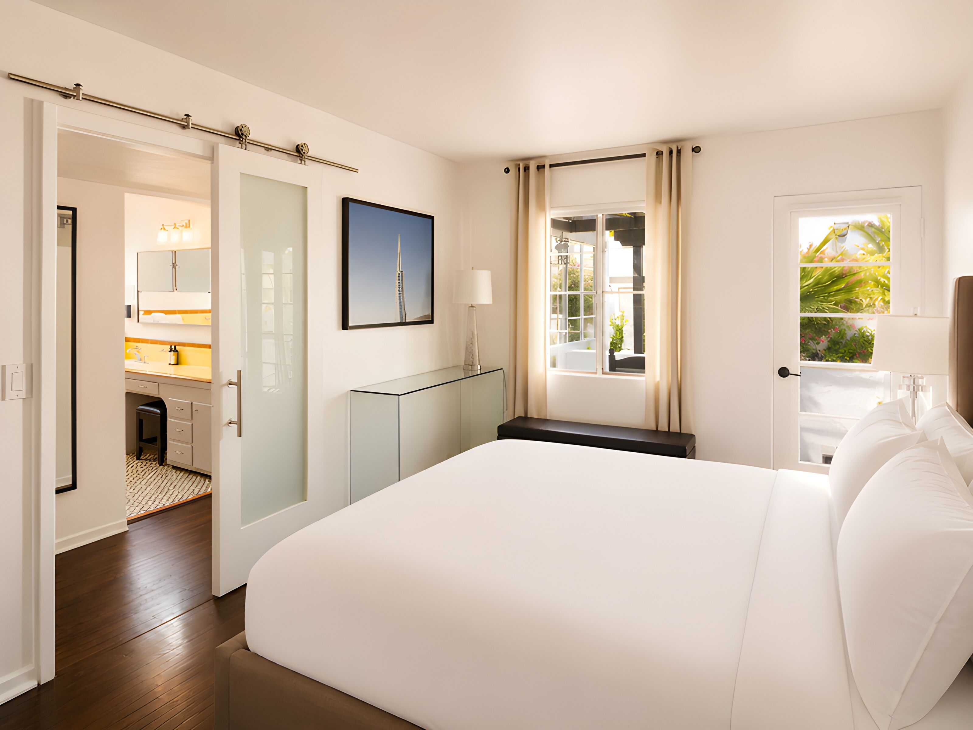 Habitación de hotel con cama, baño, vista a zonas verdes y puerta que da a otra habitación.
