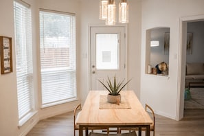 Een eetruimte met een houten tafel, stoelen, een potplant en een deur met een raam.