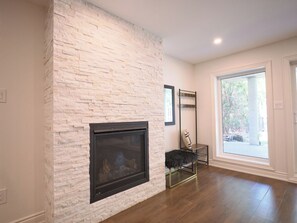 A room with a stone fireplace, a bench, and a large window.