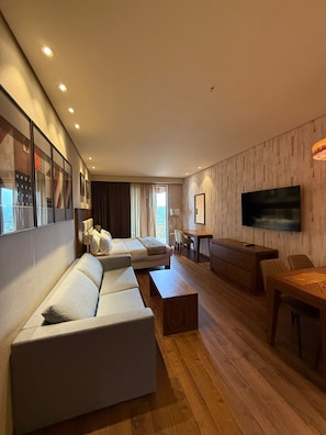 A modern living room with a sofa, coffee table, TV, and a dining area with chairs and a table.