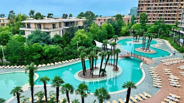 Un resort con una amplia piscina central, varias piscinas más pequeñas y numerosas tumbonas.