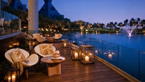 A deck with outdoor seating, a pool, and a night-time view of palm trees and distant buildings. - Luxury Retreat at The Grand Mayan – Nuevo Nayarit (Nuevo Vallarta)