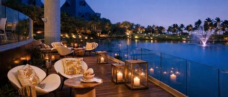 A deck with outdoor seating, a pool, and a night-time view of palm trees and distant buildings.