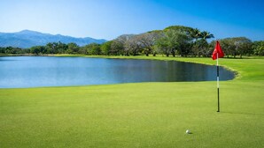A golf course with a flagstick, a pond, and trees. - Luxury Retreat at The Grand Mayan – Nuevo Nayarit (Nuevo Vallarta)