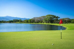 A golf course with a flagstick, a pond, and trees. - Luxury Retreat at The Grand Mayan – Nuevo Nayarit (Nuevo Vallarta)