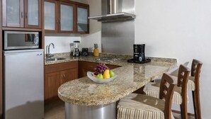A kitchen with granite countertops, wooden cabinets, a stainless steel range hood, a refrigerator, a coffee maker, and a fruit bowl. - Luxury Retreat at The Grand Mayan – Nuevo Nayarit (Nuevo Vallarta)