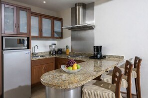 A kitchen with granite countertops, wooden cabinets, a stainless steel range hood, a refrigerator, a coffee maker, and a fruit bowl. - Luxury Retreat at The Grand Mayan – Nuevo Nayarit (Nuevo Vallarta)