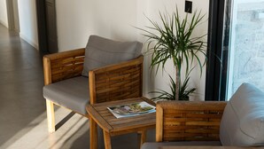 Une chaise en bois avec un coussin, une petite table en bois sur laquelle repose un magazine, et une grande plante verte.
