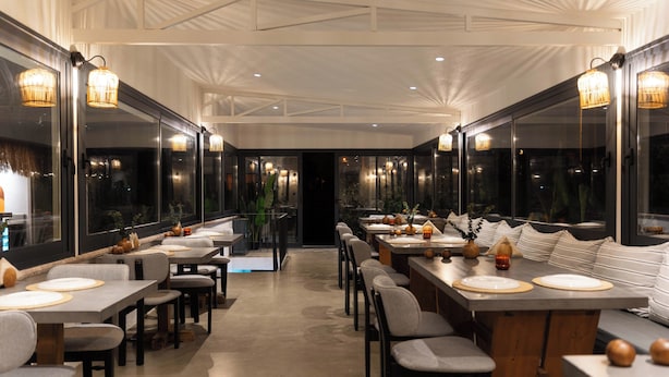 Un restaurant moderne avec de longues tables, des chaises et des luminaires suspendus.
