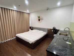 A modern hotel room with a bed, a built-in desk, a sink, and a ceiling-mounted projector. - Studio nhỏ xinh cho 1-2 người với đầy đủ tiện ích! (Hà Nội)