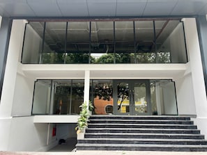 A modern building with a double-height glass facade, a staircase leading to the entrance, and a visible outdoor area with greenery. - Studio nhỏ xinh cho 1-2 người với đầy đủ tiện ích! (Hà Nội)