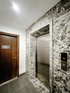 Um elevador com mostrador digital, parede de mármore e porta de madeira com uma placa.