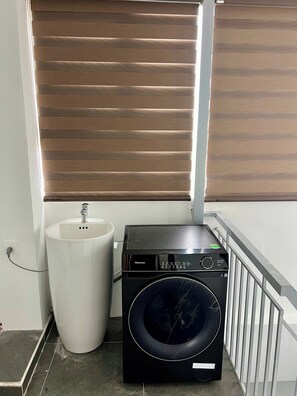 A compact laundry area with a washing machine, a sink, and a window with blinds. - Studio nhỏ xinh cho 1-2 người với đầy đủ tiện ích! (Hà Nội)