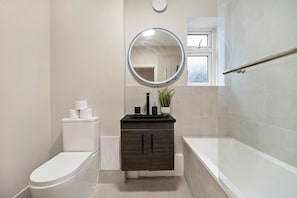 A bathroom with a toilet, a sink with a mirror above it, a bathtub, and a window. - Spacious 3-Bed Apartment • Sleeps 6 • Free Parking • 15mins to Central London (London)
