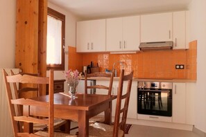 A kitchen with white cabinets, a wooden dining table, chairs, a vase with flowers, a stove, and an oven. - Les Lilas Apartment (2–4 people) (BASSURELS)