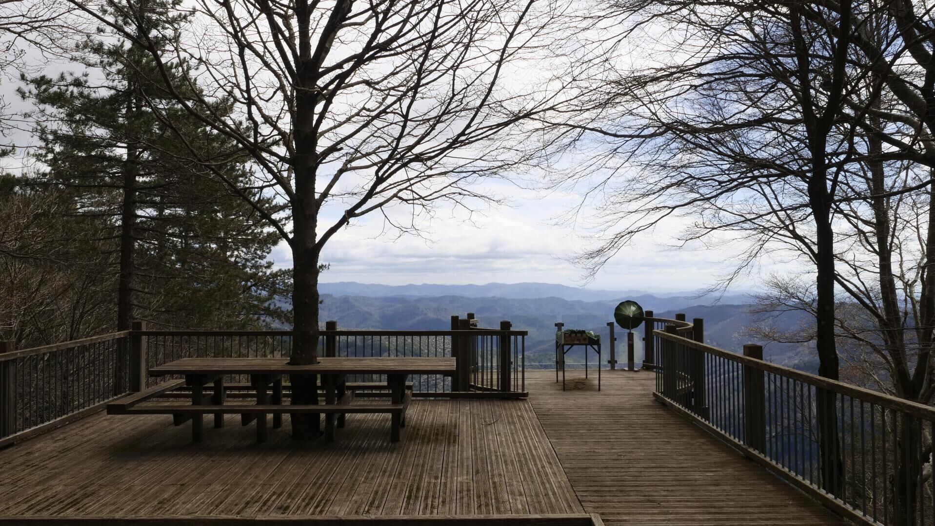 Eine Holzterrasse mit einer Bank, einem Wegweiser und Blick auf Berge.