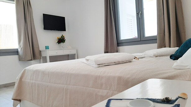 Hotellihuone, jossa on sänky, yöpöytä, seinälle asennettu televisio ja ikkuna, jossa on verhot.