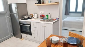 Kompakti keittiö, jossa on jääkaappi, uuni ja pesuallas, ruokailutila kahdelle katetulla pöydällä sekä sänky viereisessä huoneessa.