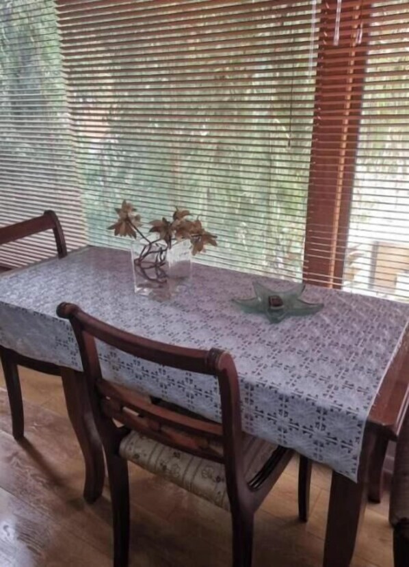 Ein Esstisch mit einer Spitzenleinentischdecke, zwei Holzsesseln und einer Vase mit getrockneten Blumen.