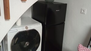 Een gezellig, compact leefruimte met een wasmachine, een koelkast, een houten stoel en een gestreept kussen.