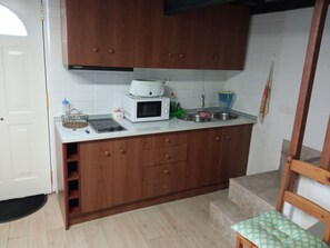 Cozinha com armários de madeira, micro-ondas, pia e uma cadeira.