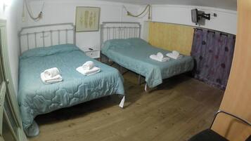Habitación con dos camas, cada una con una colcha verde azulada y toallas blancas. El suelo es de madera, hay un radiador blanco y un televisor montado en la pared.