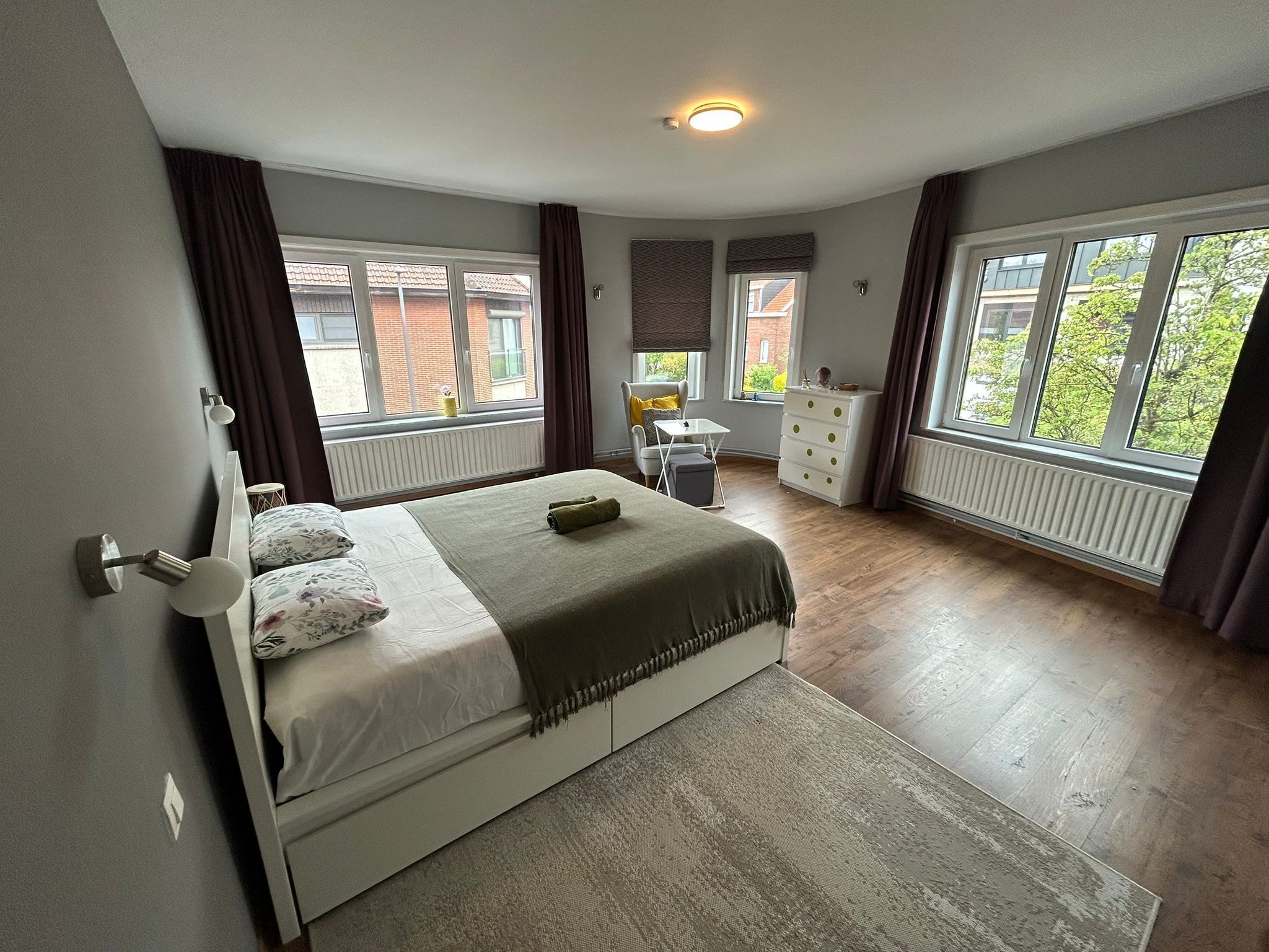Ein Schlafzimmer mit einem Bett, einem Schreibtisch, einem Sessel und großen Fenstern.