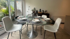 A dining area with a glass table, white chairs, and a view of greenery outside.