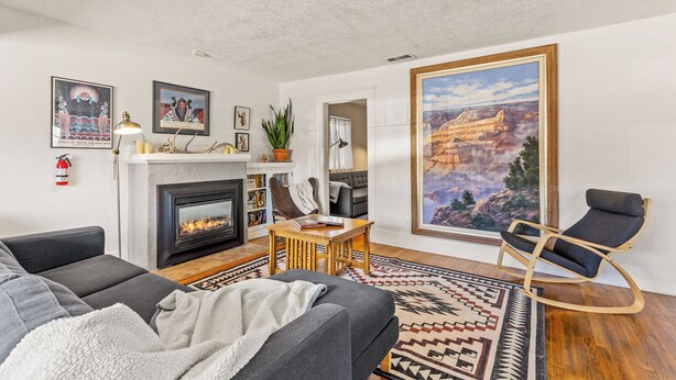 A living room with a fireplace, a sofa, a rocking chair, and a large painting of a mountain landscape. - Route 66/Grand Canyon Retreat, Central Williams, Family-friendly, Sleeps 8 (Williams)