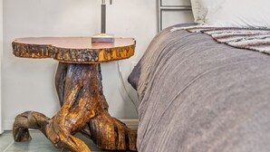 A bedroom with a metal bed frame, a bedside table with a lamp, and a large wooden sculpture. - Route 66/Grand Canyon Retreat, Central Williams, Family-friendly, Sleeps 8 (Williams)