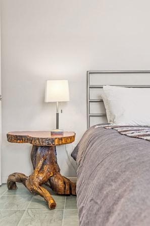 Un dormitorio con estructura de cama metálica, mesita de noche con lámpara y una gran escultura de madera.