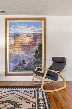A room with a framed painting of a canyon landscape, a rocking chair, and a patterned rug. - Route 66/Grand Canyon Retreat, Central Williams, Family-friendly, Sleeps 8 (Williams)
