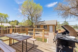A wooden deck with picnic tables, a barbecue grill, and a small wooden building in the background. - Route 66/Grand Canyon Retreat, Central Williams, Family-friendly, Sleeps 8 (Williams)