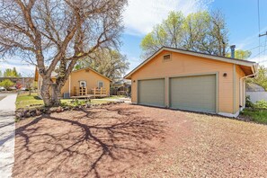 A residential garage with a brown exterior and a green garage door, surrounded by a gravel driveway and trees. - Route 66/Grand Canyon Retreat, Central Williams, Family-friendly, Sleeps 8 (Williams)