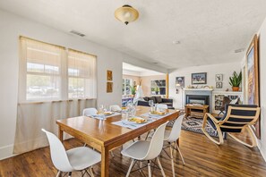 A dining area with a wooden table, white chairs, and a fireplace in the background. - Route 66/Grand Canyon Retreat, Central Williams, Family-friendly, Sleeps 8 (Williams)
