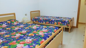 Two single beds with floral bedding, a bedside table with a lamp, and a plain white wall. - Apartment with fireplace and view of the Orfento Valley (Caramanico Terme)