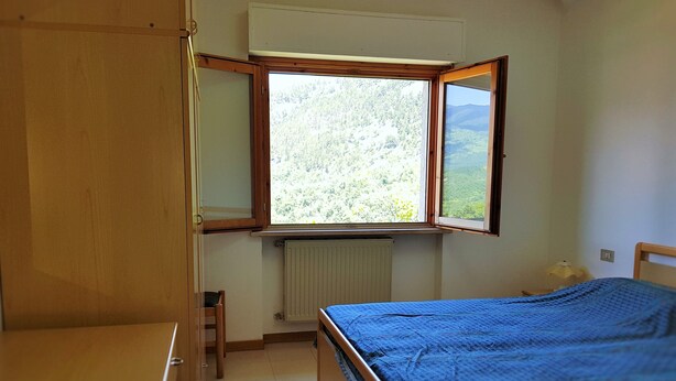 A bedroom with a bed, a window, a radiator, and a wooden wardrobe. - Apartment with fireplace and view of the Orfento Valley (Caramanico Terme)