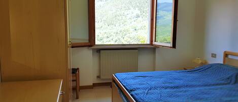 A bedroom with a bed, a window, a radiator, and a wooden wardrobe.