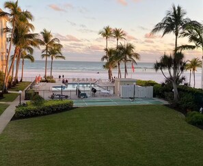 Ein Poolbereich mit Blick auf Strand und Meer, umgeben von Palmen und einem Zaun.