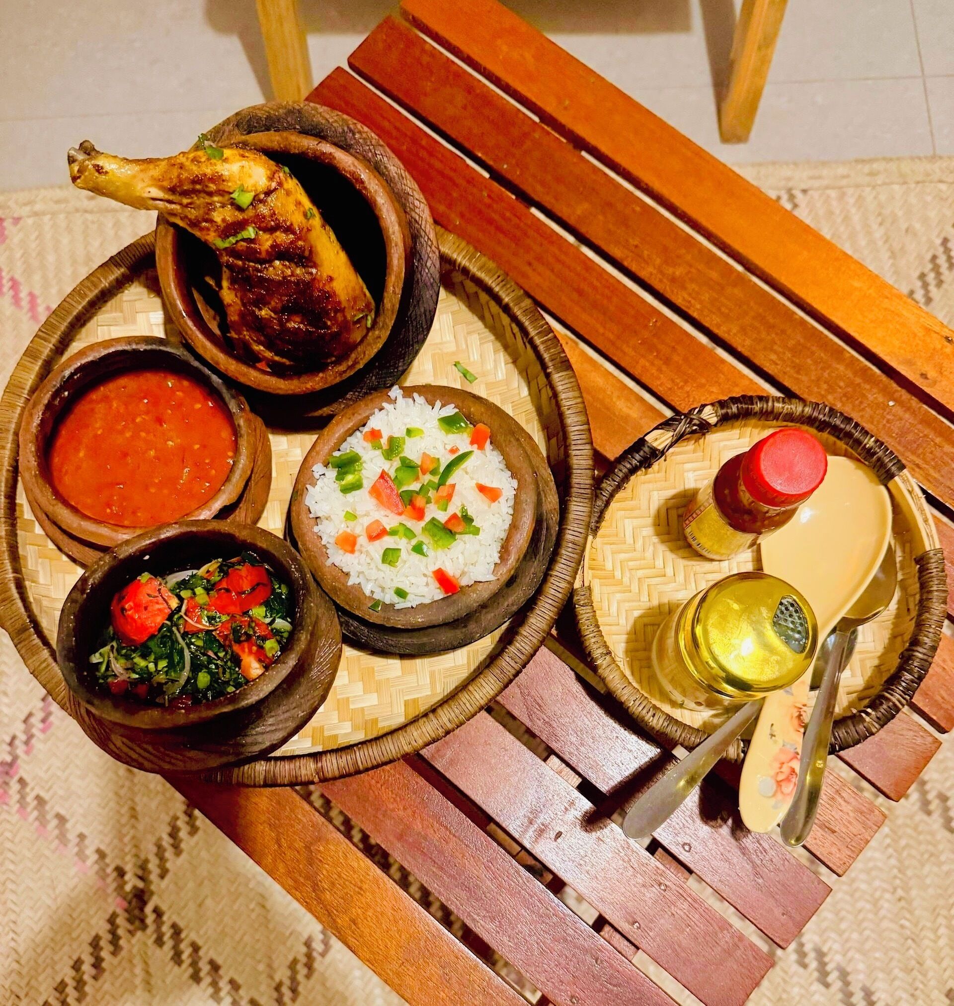 Una mesa de madera con varios platos, incluyendo arroz, sopa y un muslo de pollo a la parrilla.