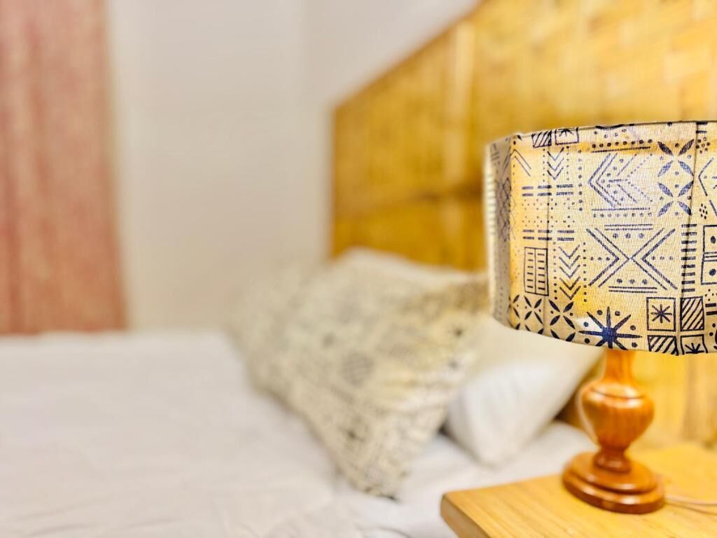 En seng med et mønstret sengegavl, en senget lampe og en pude.
