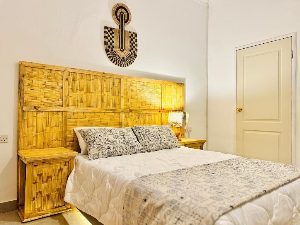 Una habitación con cama, cabecera de madera, dos mesitas de noche y una puerta.